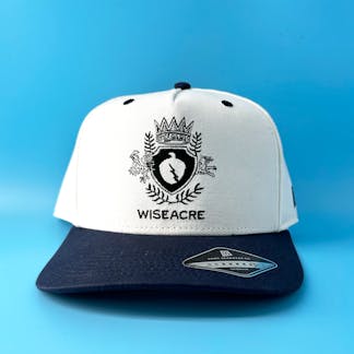 off white and navy hat with wiseacre crest on a blue background