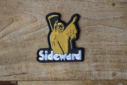 An embroidered black patch featuring a yellow grim reaper holding peace signs with the text "Sideward" underneath.