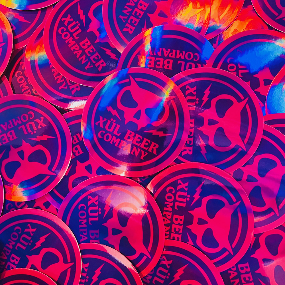 Circle holographic sticker that is purple and pink and features our fanghead logo.