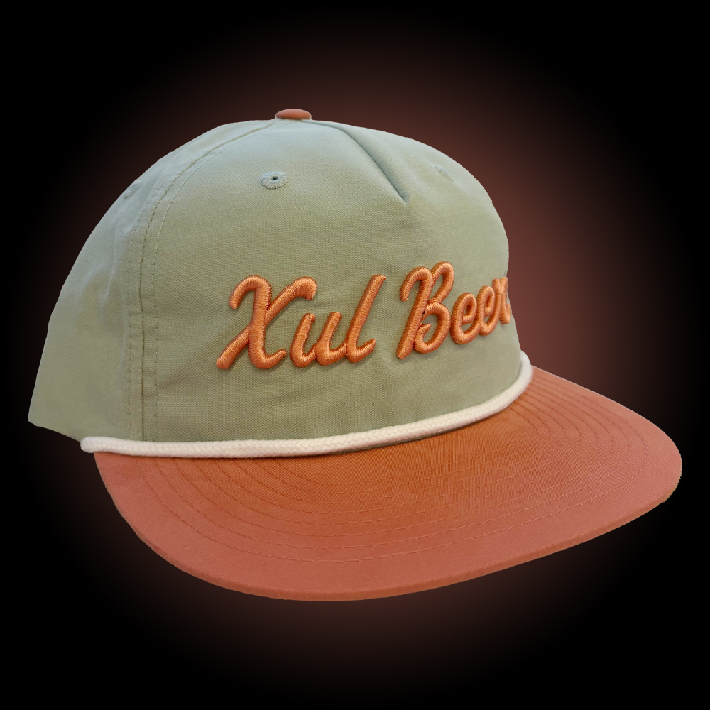 Xul Beer seafoam hat with salmon colored bill and white string.