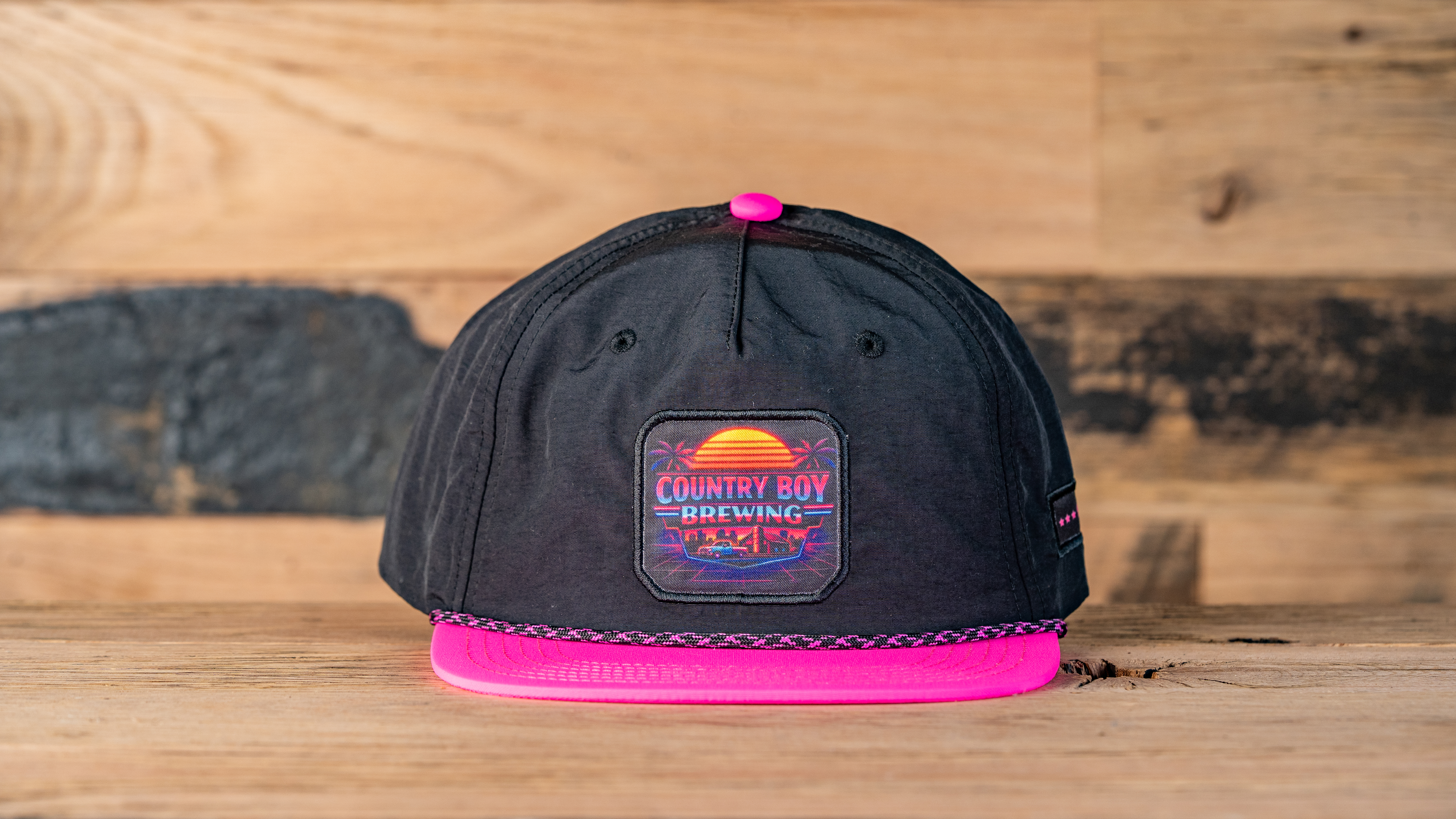 Black hat, pink brim, Country Boy Brewing logo on square patch with sunset over ocean.
