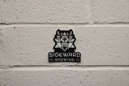 a sticker of Sideward Brewing's logo, which resembles a demon cow skull with a triangle and circle behind it, with the Sideward Brewing wordmark below.