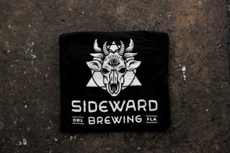 A black tee featuring a white Sideward Brewing logo, which resembles a demon cow skull with a triangle and circle behind it, with the Sideward Brewing wordmark below.