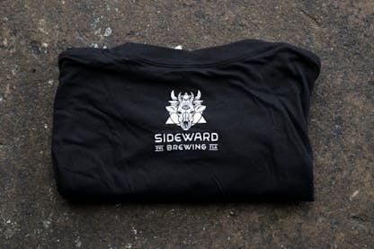 The backside of the black Moon Boots tee - featuring the Sideward Brewing logo + wordmark right between the shoulders.
