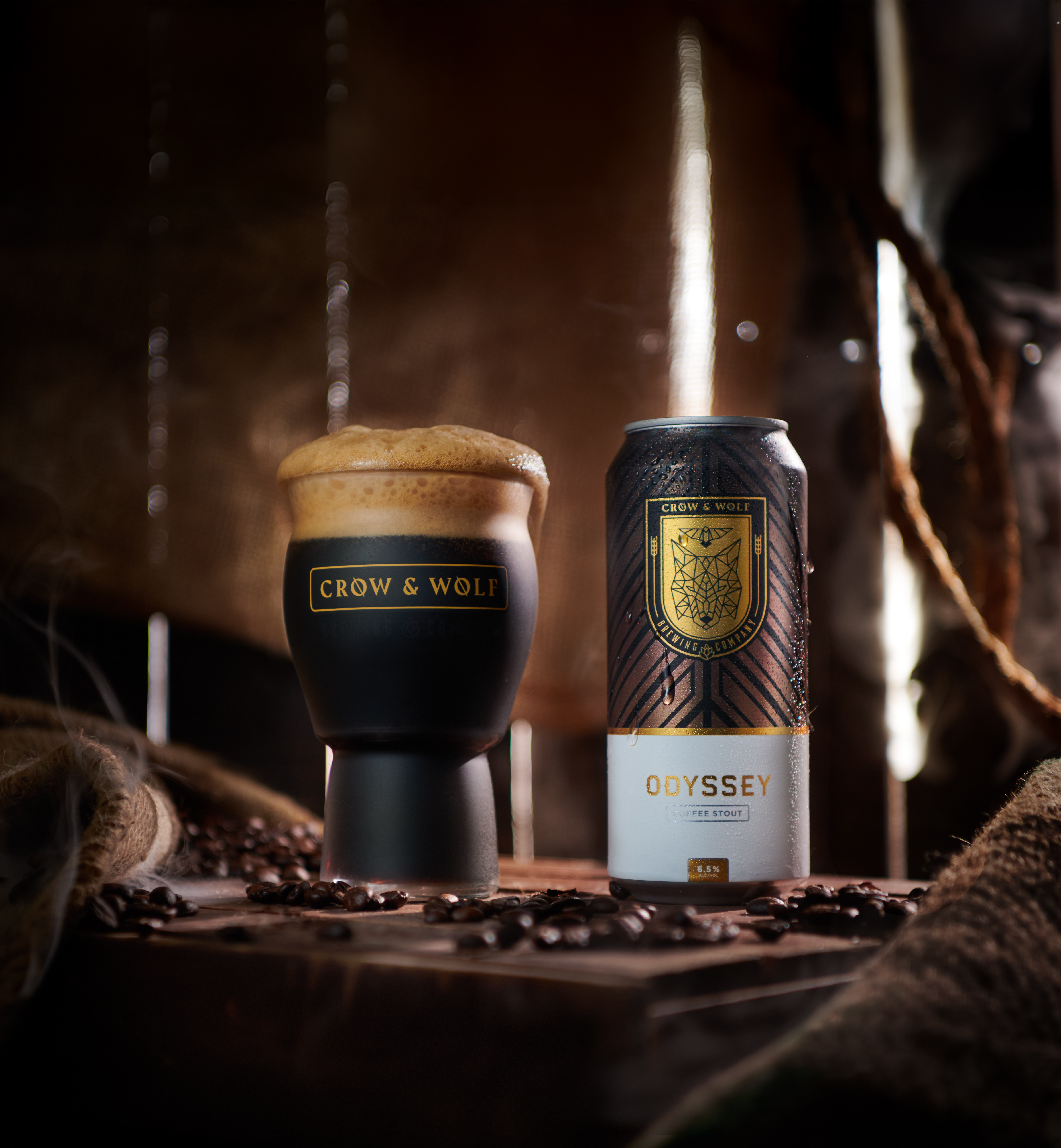 a fresh pint of odyssey with foam next to a can with some coffee beans in the foreground and light peaking in the back