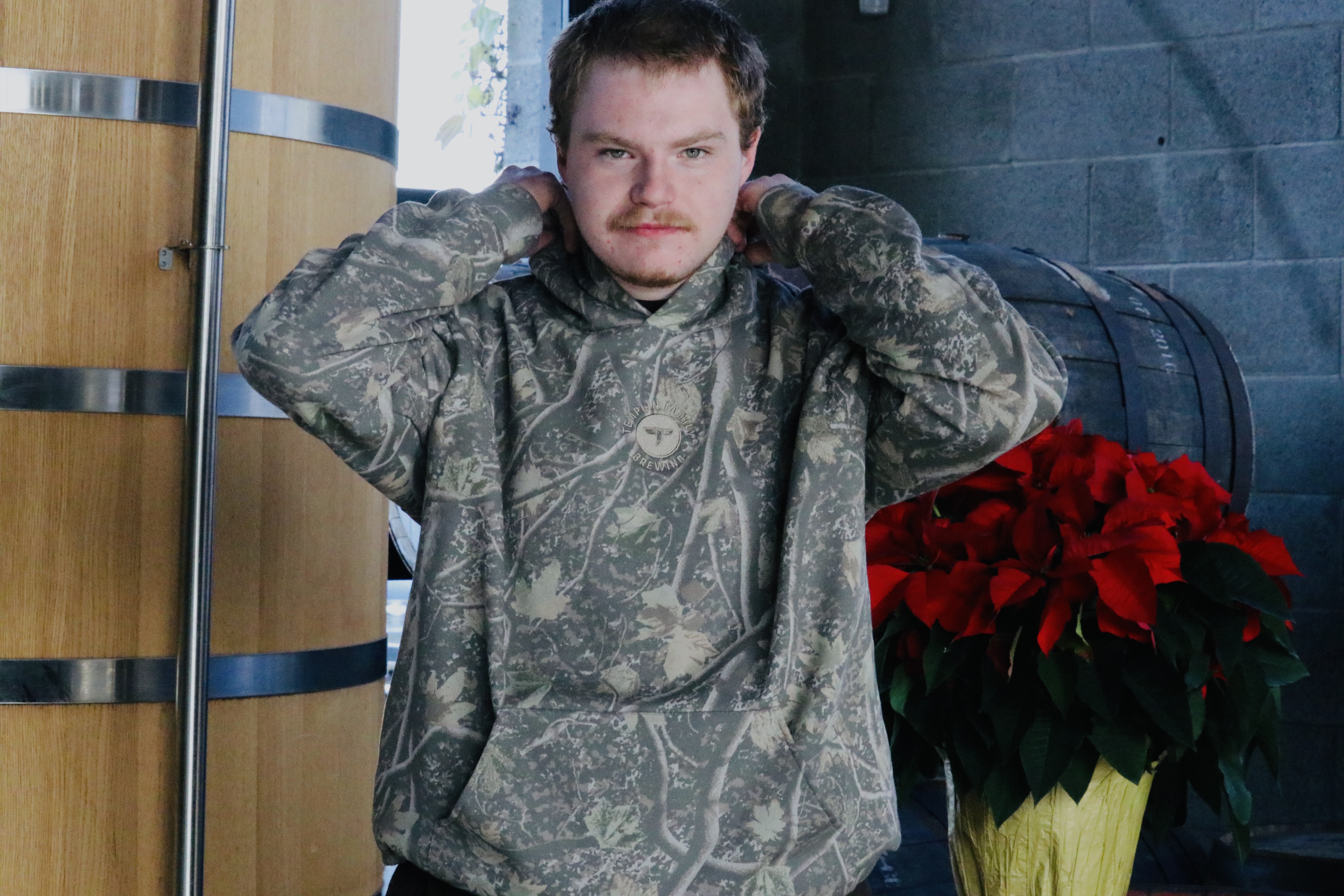 A guy wearing our camo hoodie with a company logo centered on chest. The thread of the logo is subtle, blending in with the camo fees. For sale on our website, listed at $72 plus tax.