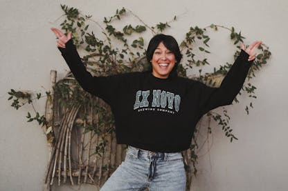 Women wearing black cropped crew neck pullover fleece with large white and teal EX NOVO BREWING COMPANY written across the chest
