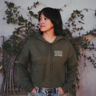 women wearing olive green crop hooded sweatshirt that says "Drink Beer Do Good" on left chest in cream color.