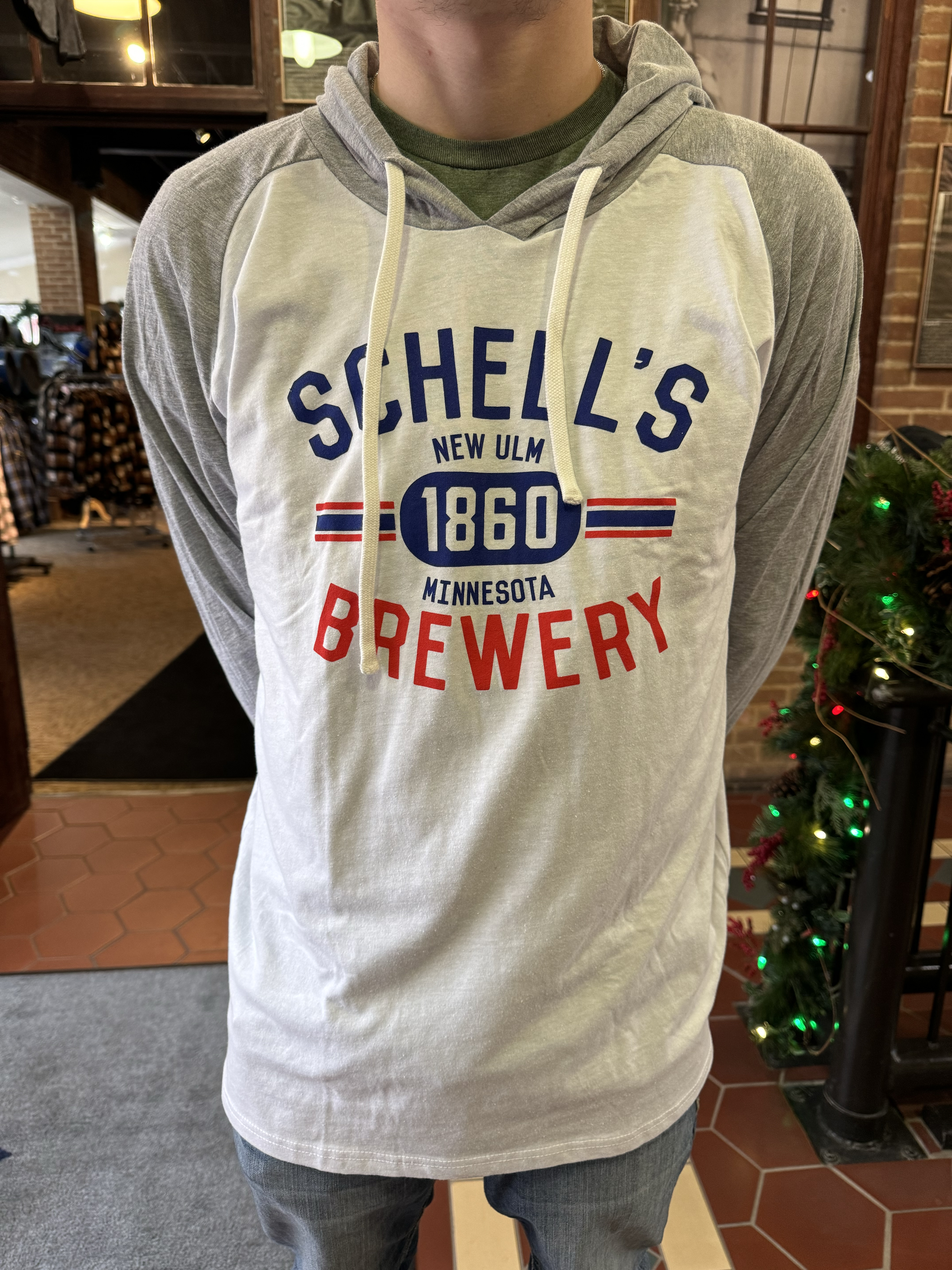 White hoodie with grey sleeves and a red, white, and blue Schell logo on front.