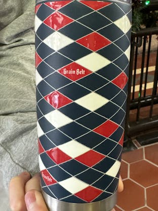 Blue tumbler with red and white diamonds wrapped around with Grain Belt logos.