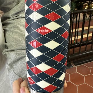Blue tumbler with red and white diamonds wrapped around with Grain Belt logos.