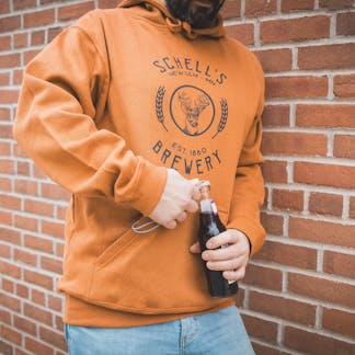 Copper colored sweatshirt with Schell logo on front and a bottle coozie in front pocket.