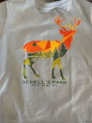 Blue colored kids shirt with deer and Schell park logo on front.