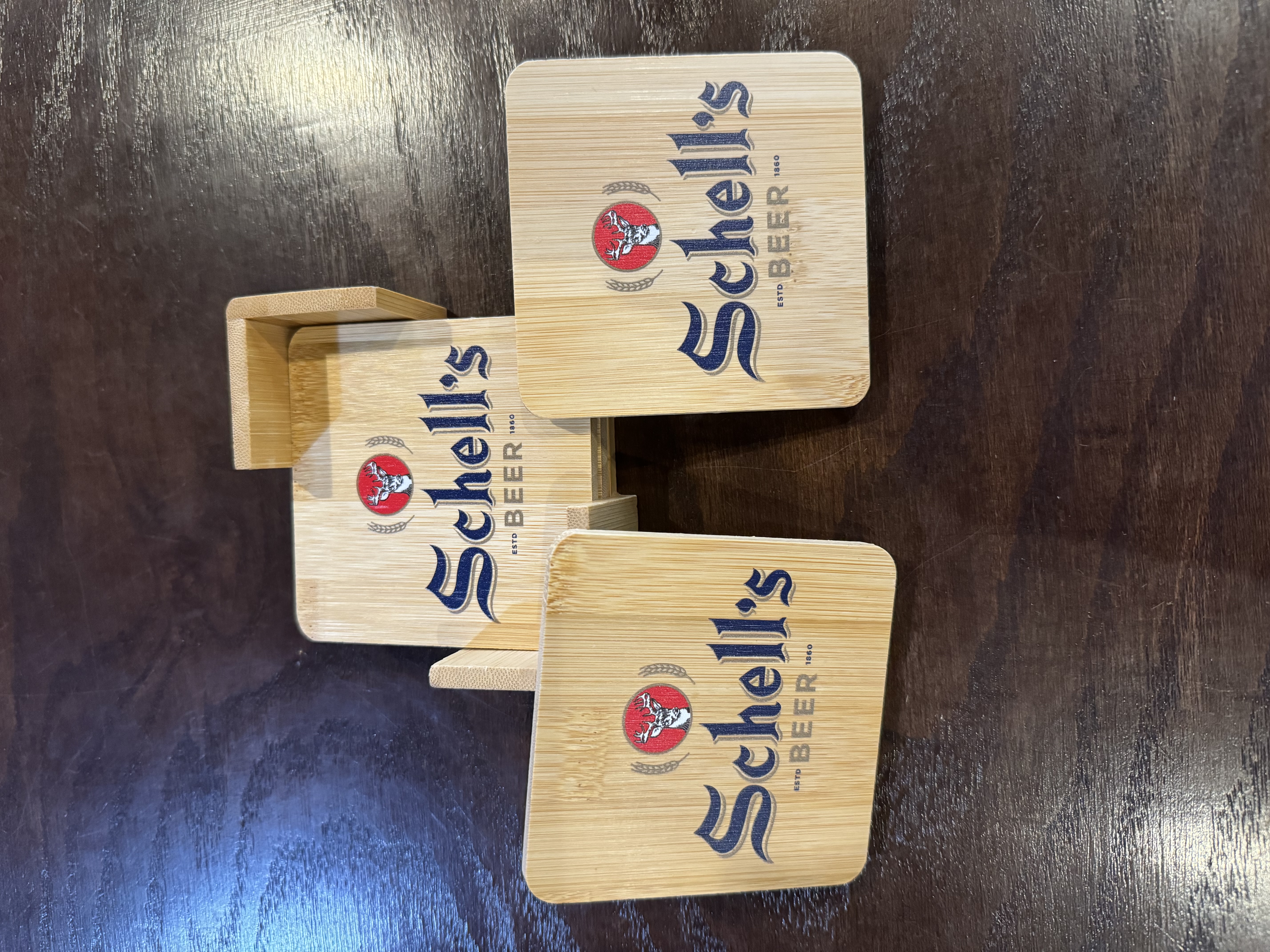 Four wooden coasters with holder and Schell logo printed on the top.