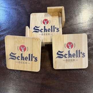 Four wooden coasters with holder and Schell logo printed on the top.