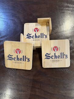 Four wooden coasters with holder and Schell logo printed on the top.