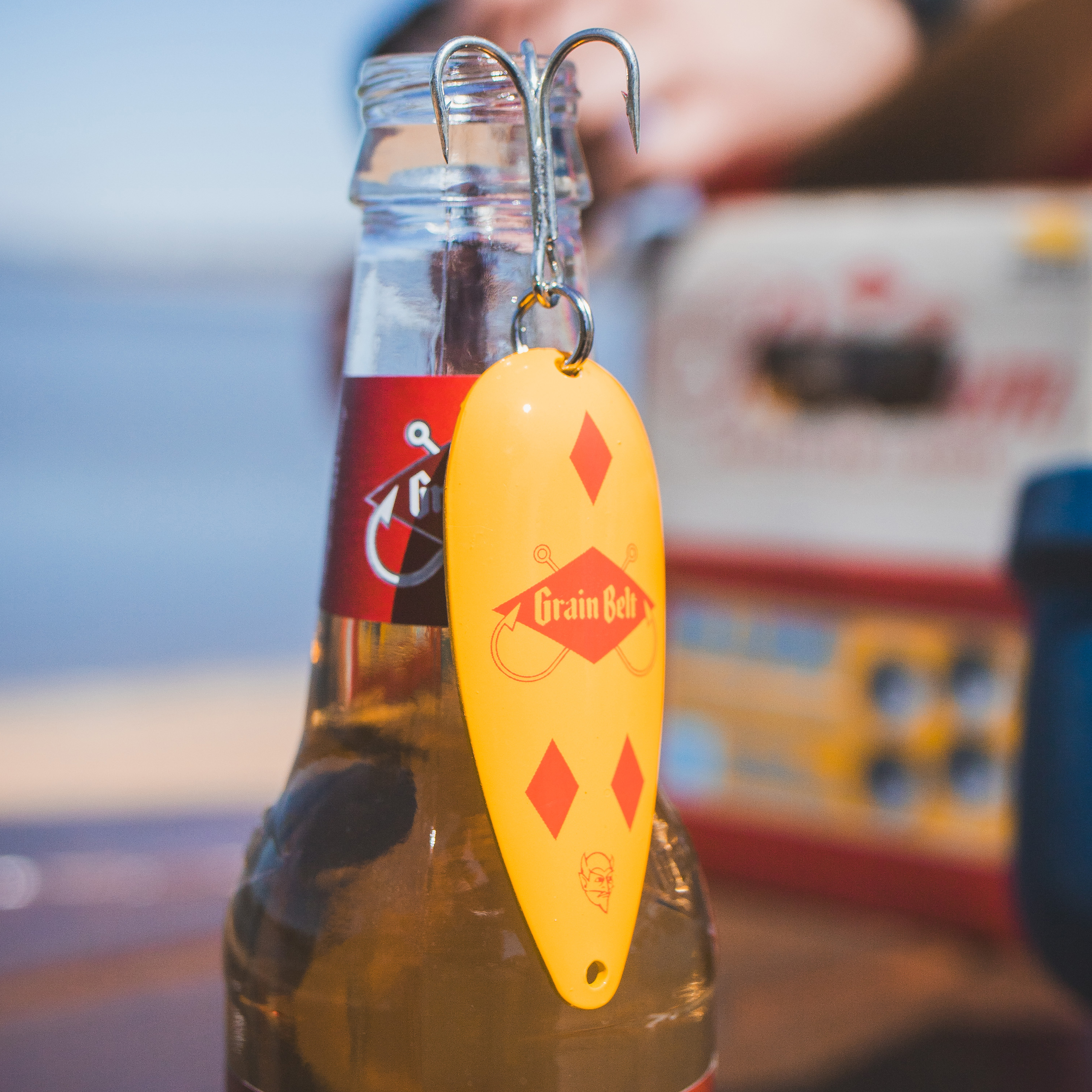Red and yellow fishing lure with treble hook and Grain Belt logo.