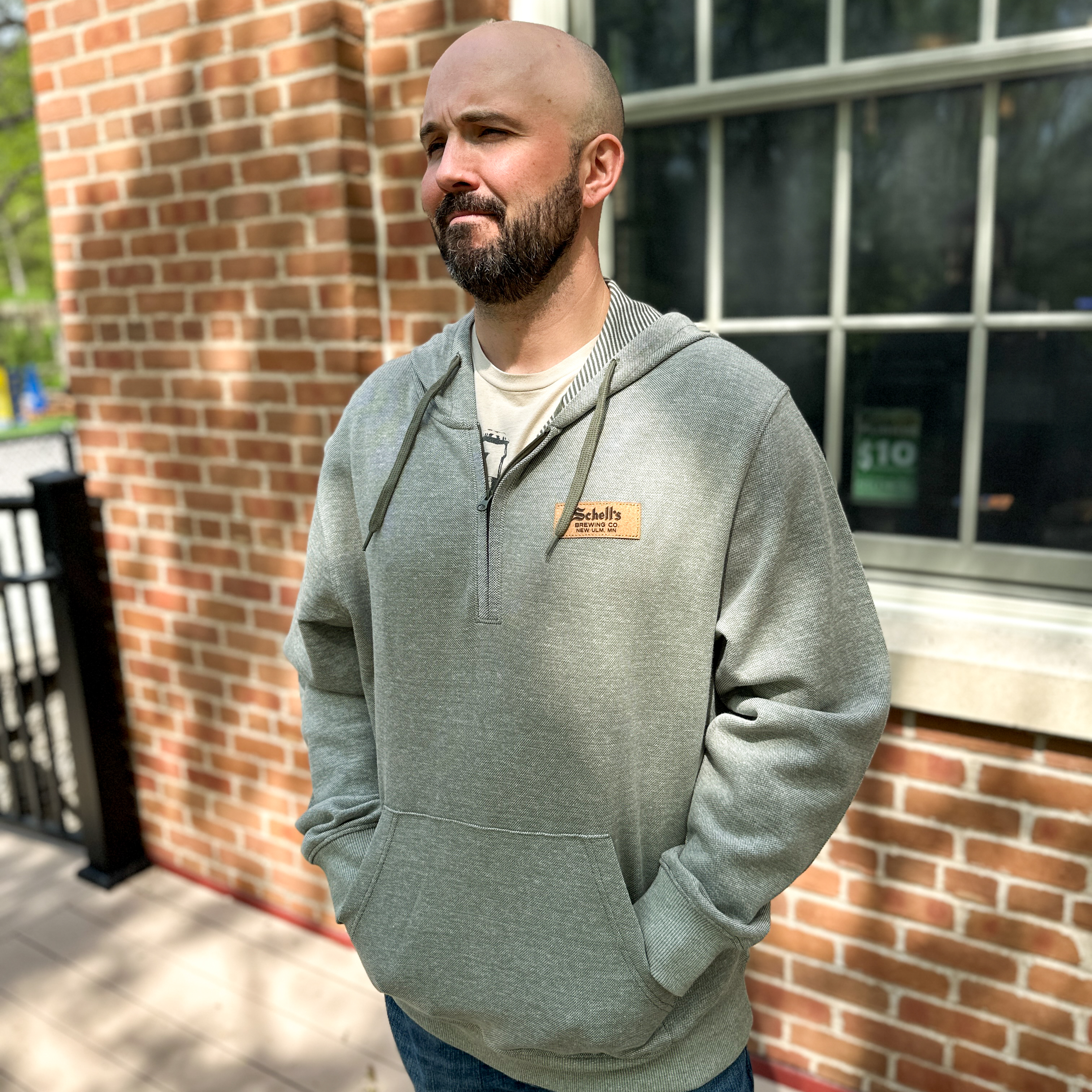 Heather green hooded quarter zip sweatshirt with cork Schell patch on the left lapel.