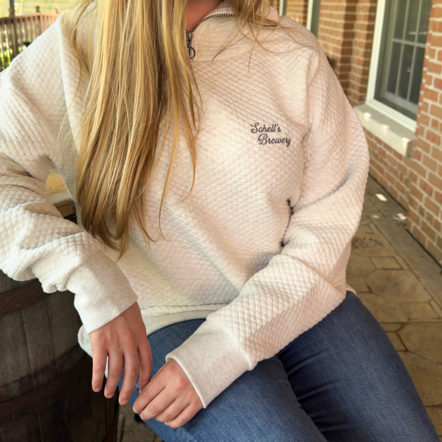 Oatmeal colored quarter zip sweatshirt with Schell logo on the front left lapel.