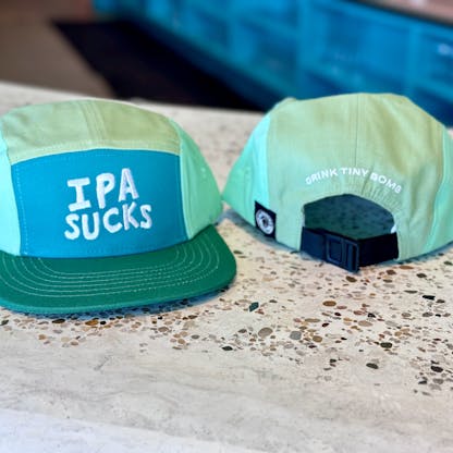 a blue and green hat that reads "IPA SUCKS" on the front and "Drink Tiny Bomb" on the back