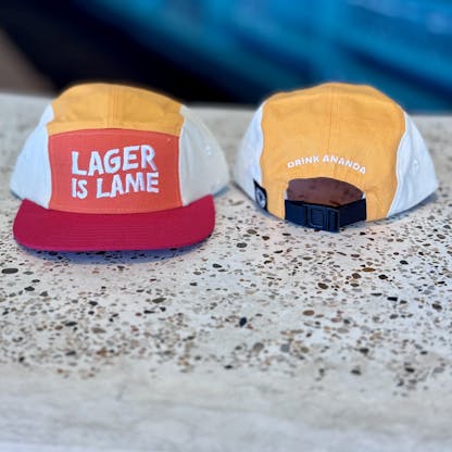 a red and orange hat that says "LAGER IS LAME" on the front and "drink ananda on the back"
