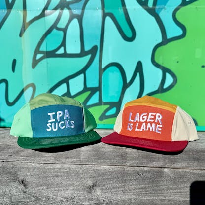 a blue and green hat that reads "IPA SUCKS" next to a red and orange hat that says "LAGER IS LAME"