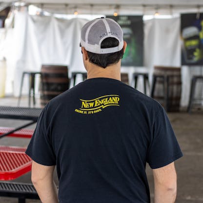 Back image of male model in black t-shirt with yellow New England Brewing Company logo on top center of shirt