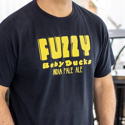 Close-up image of black t-shirt with yellow Fuzzy Baby Ducks logo on chest
