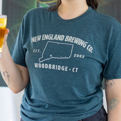 Close-up image of female model holding a beer wearing short sleeve blue "Woodbridge, CT" T-shirt