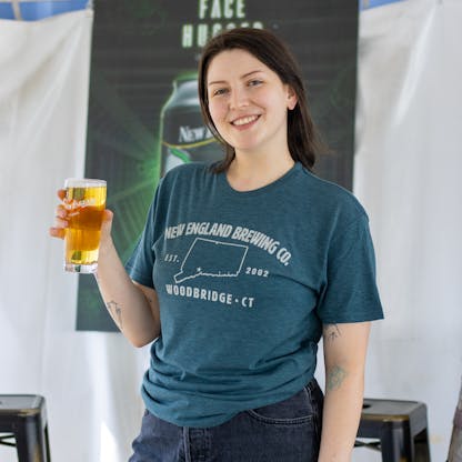 Female model holding a beer wearing short sleeve blue "Woodbridge, CT" T-shirt