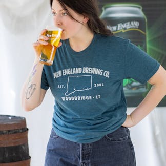 Female model drinking a beer wearing short sleeve blue "Woodbridge, CT" T-shirt