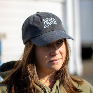 Female model wearing black NEBCO state logo dad hat with white embroidery