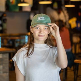 Female model wearing green NEBCO state logo dad hat with white embroidery