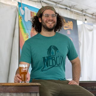 male model sitting with beer wearing green nebco x sea hag t shirt