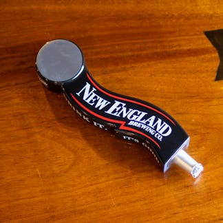 Image of branded New England Brewing tap handle on table