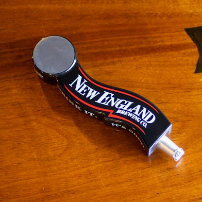 Image of branded New England Brewing tap handle on table