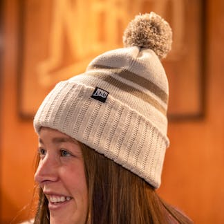 Female model smiling wearing tan hat with pom