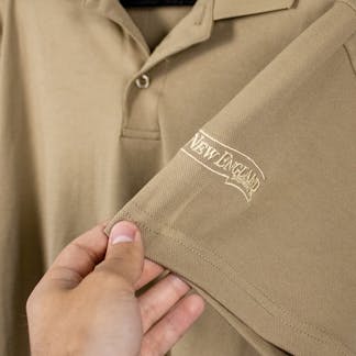 close up of embroidered New England Brewing Company swoosh logo on khaki shirt