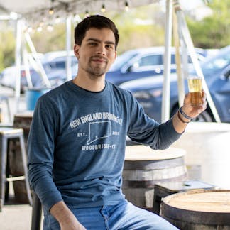 Male model holding beer wearing long sleeve blue "Woodbridge, CT" T-shirt