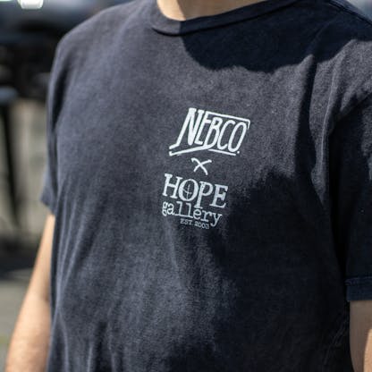 Close up of black t-shirt with NEBCO state x Hope Gallery logos on left chest