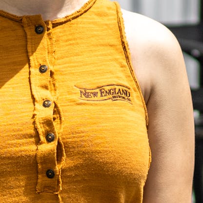 Close up of New England Brewing Company logo on yellow women's tank left chest