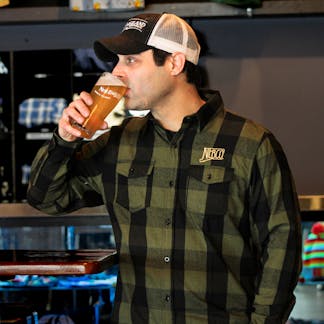 Male model smiling wearing army green & black buffalo flannel drinking a beer