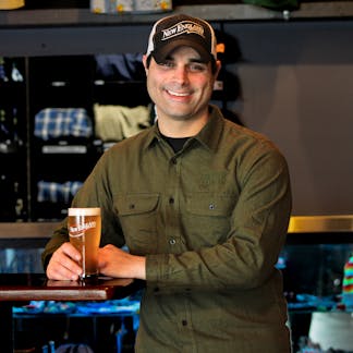 Male model smiling wearing army green flannel holding a beer