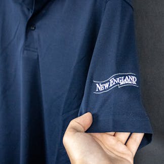 close up of embroidered New England Brewing Company swoosh logo on navy shirt