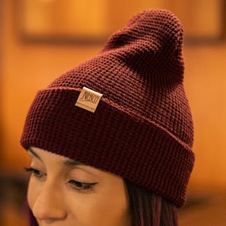 Female model wearing maroon waffle knit winter hat with leather applique NEBCO logo on cuff