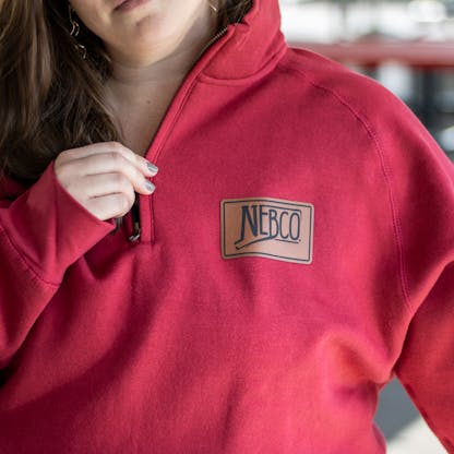Close up of NEBCO State logo leather applique on red quarter zip