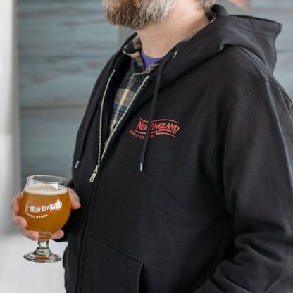 Close-Up of red New England Brewing Logo on zip up hoodie being worn by male model
