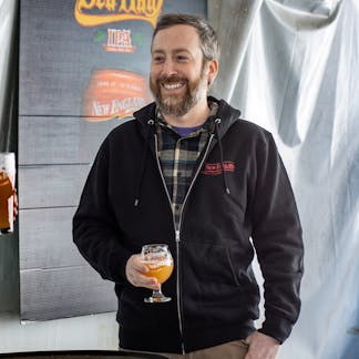 Smiling Male model wearing black zip up sweatshirt holding a beer