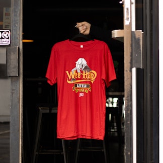 Red Wee Hag t-shirt suspended on hanger in contrasting dark doorway