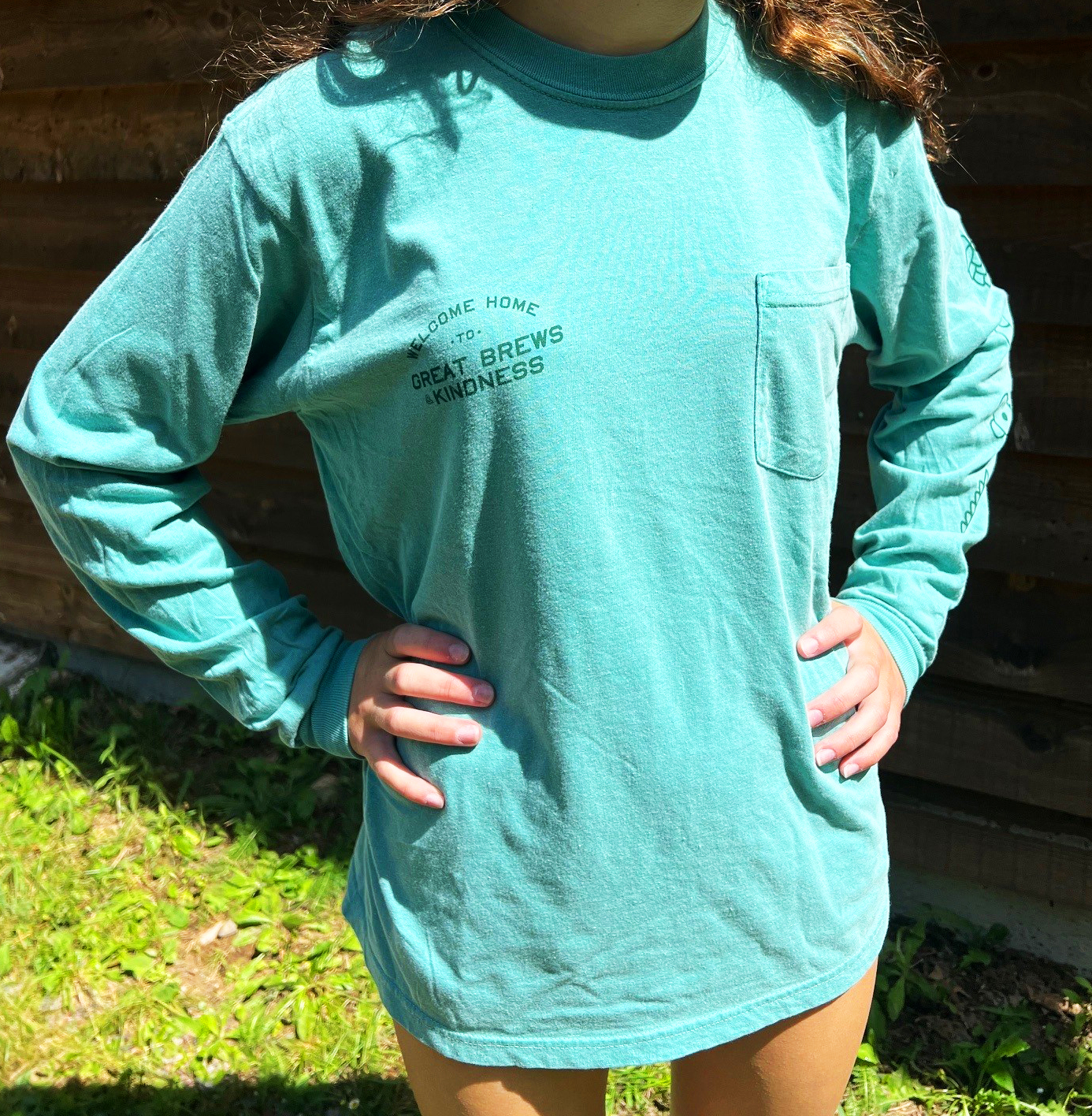 person modeling long sleeve t-shirt, seafoam color with pocket on left chest and branding on right chest
